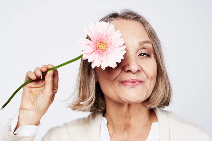 Older woman holding a flower over her eye